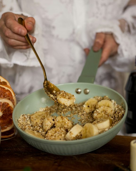 Hands stirring sliced bananas and oats in a light green pan