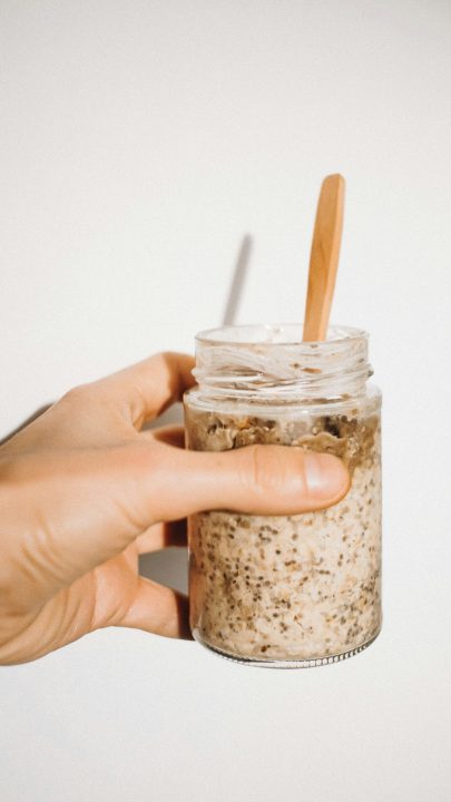 Hand holding a prepped breakfast jar with a wooden spoon, ready for a busy morning