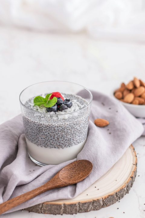 A glass of chia seed pudding topped with blueberries and raspberries, with a spoon
