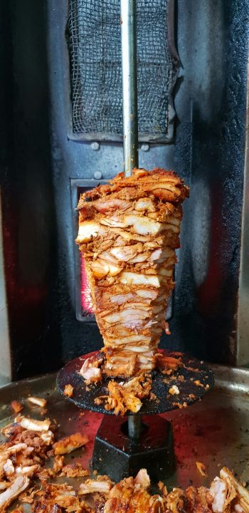 Spiced chicken shawarma roasting on a vertical rotisserie spit