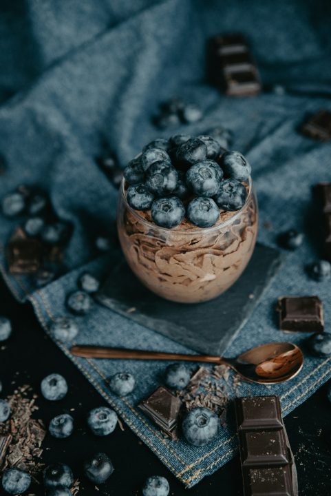 A bowl of creamy chocolate topped with blueberries on a cloth