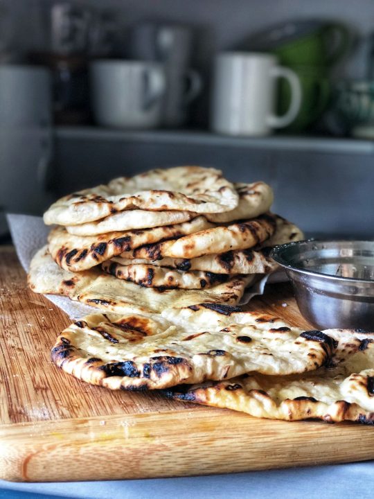 A pile of homemade flatbreads with olive oil and garlic on a wooden cutting board