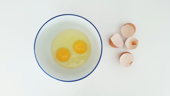Two cracked eggs in a mixing bowl beside the eggshells