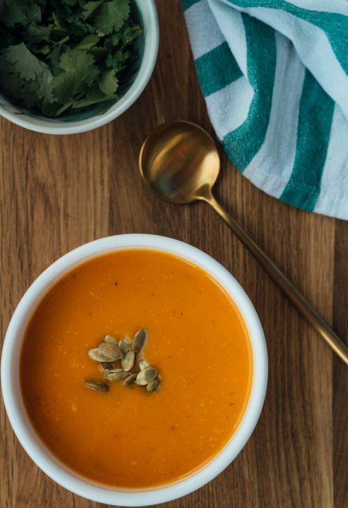 A brown wooden spoon with smooth orange soup