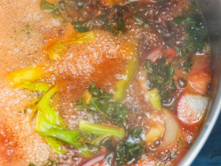 Vegetable soup simmering in a pot with kale, celery and tomato chunks