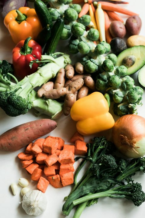 Assorted fresh vegetables including broccoli, peppers, brussels sprouts and potatoes on a white surface