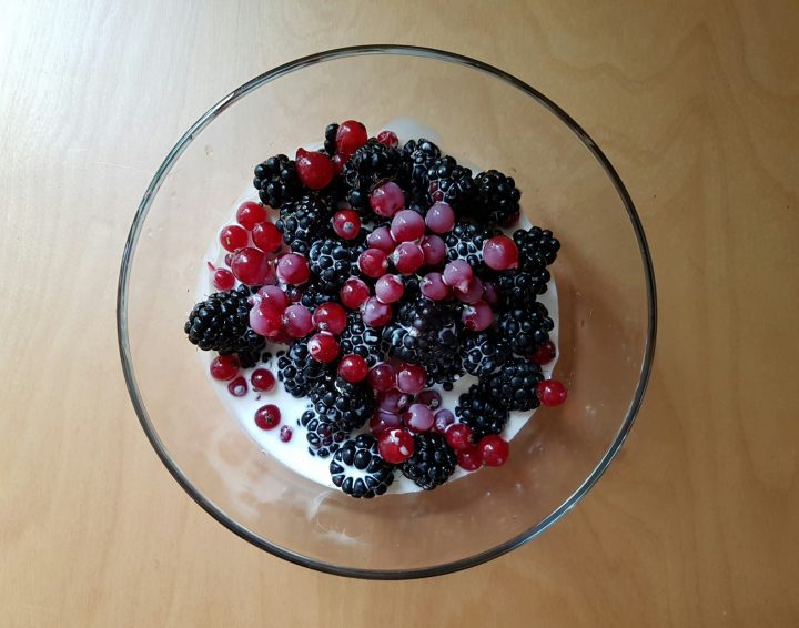 A glass bowl filled with yogurt topped with blueberries and raspberries