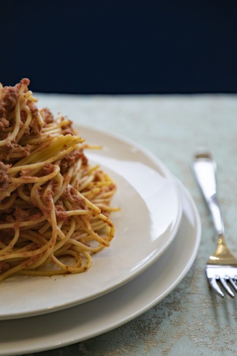 A white plate topped with spaghetti and ground meat bolognese sauce