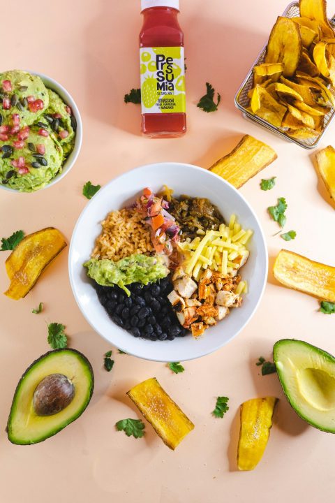 A bowl of Mexican-style food next to a bowl of guacamole, similar to a beef taco rice bowl