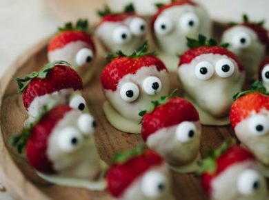 A wooden plate topped with strawberries decorated with googly eyes, a simple healthy Halloween snack
