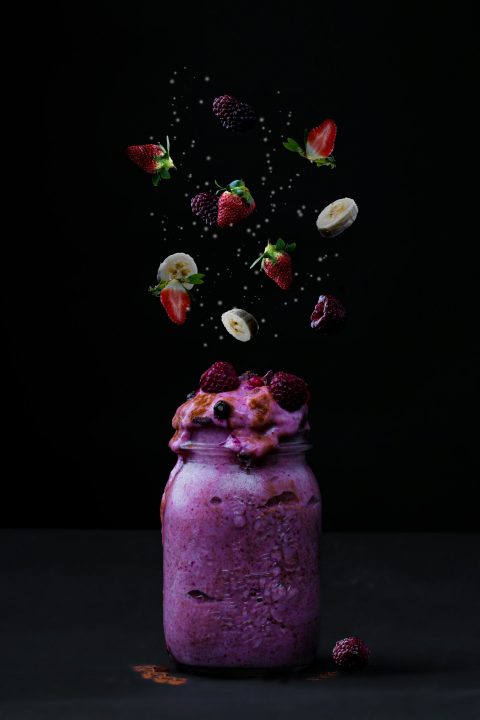 A purple smoothie in a glass jar with floating strawberries, bananas and blackberries