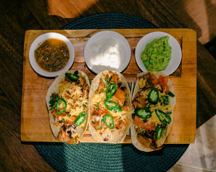 Three tacos on a cutting board with salsa and guacamole