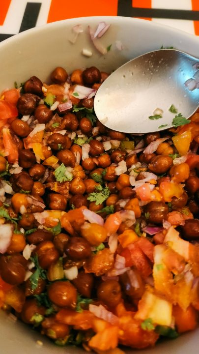 A bowl of chana chaat with chickpeas, chopped tomatoes, onions and cilantro