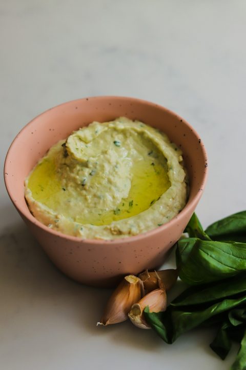 A bowl of homemade hummus next to garlic cloves