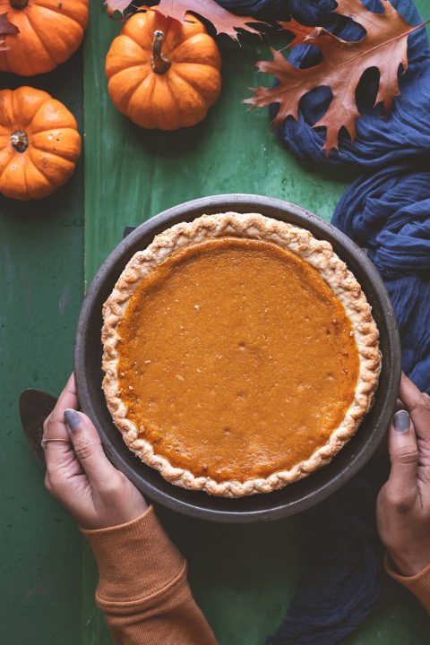 A person holding a pumpkin pie over a green table
