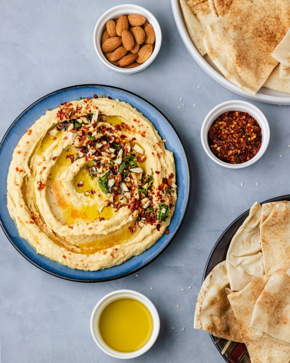A plate of hummus served with pita bread and a small bowl of olive oil