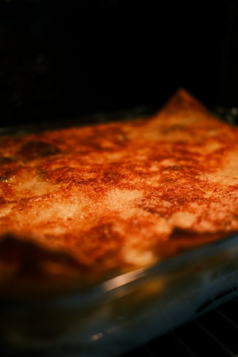 A golden brown baked lasagna in a glass dish inside a dark oven