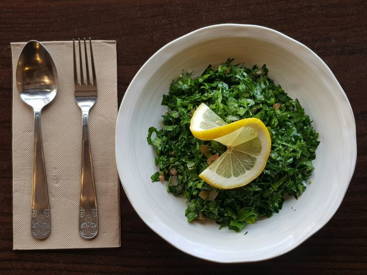Parsley tabbouleh with diced tomato and onion in a white bowl, topped with a lemon slice