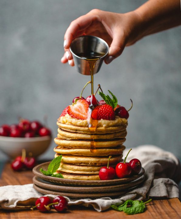 Person pouring syrup on a stack of pancakes
