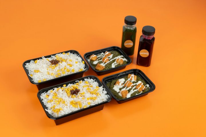 Four meal prep containers of food on an orange surface