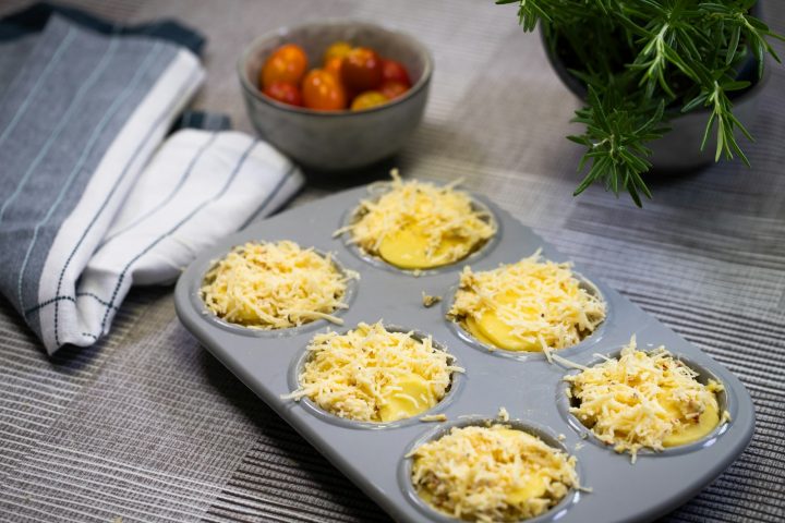 A muffin tin filled with cheese next to a bowl of fruit