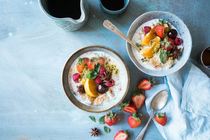 Two bowls of oatmeal topped with fruit next to coffee
