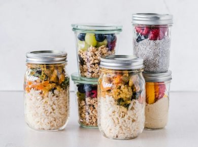 Six full glass meal prep jars with breakfast and lunch on a white surface