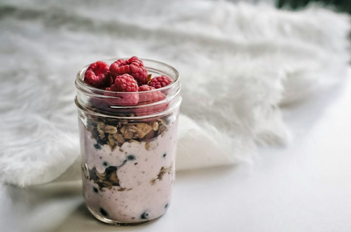 Mason jar layered with granola, yogurt and raspberries