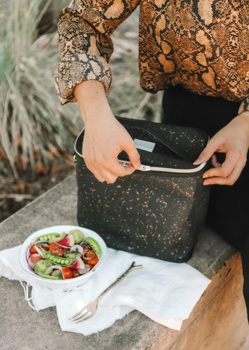 Woman opening a lunch bag next to a bowl of salad