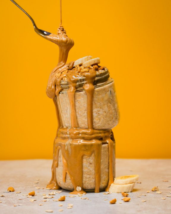 Peanut butter drizzled over stacked jars of oatmeal with bananas