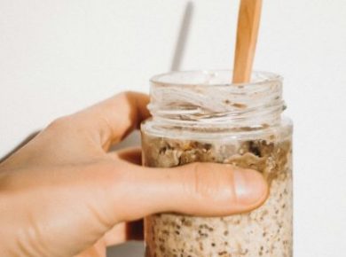 A hand holding a jar of overnight oats with a wooden spoon in it