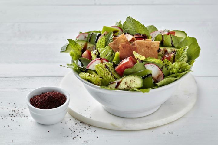 A white bowl filled with salad next to a small bowl of dressing