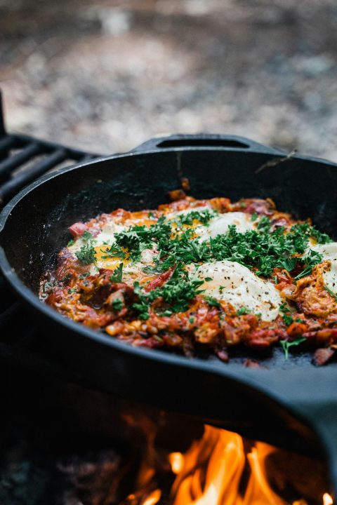 Eggs cooking in tomato sauce in a cast-iron skillet over a campfire