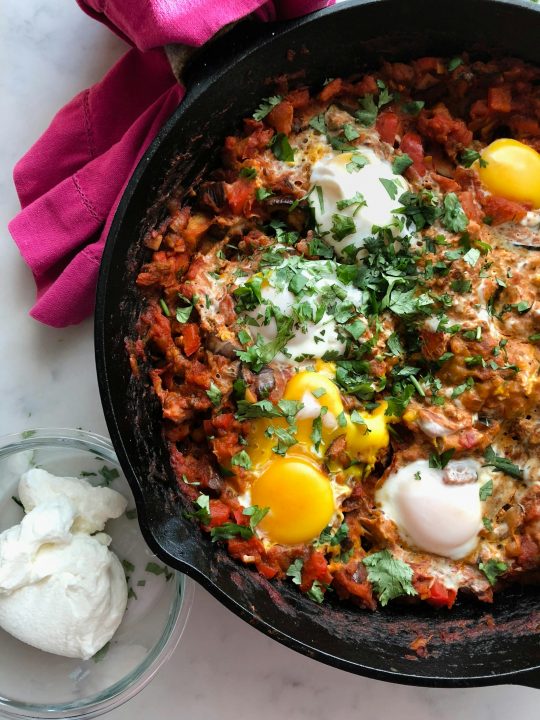 Shakshuka with red peppers and tomatoes cooking in a skillet