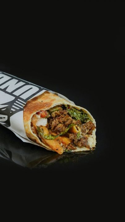 A wrapped beef shawarma sandwich on a dark background