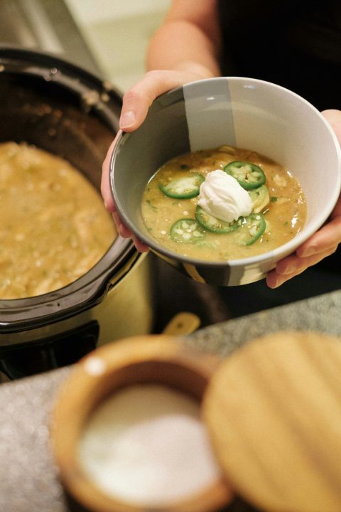 A person holding a bowl of soup in front of a crock pot