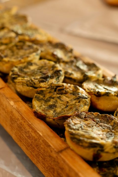 Small spinach quiches arranged in a row on a wooden serving tray