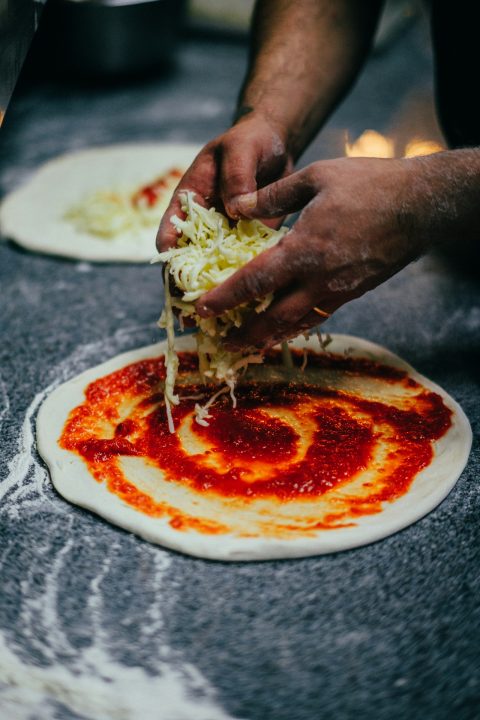 A person spreading tomato sauce on a pizza