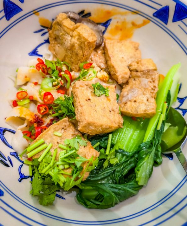 Noodle bowl topped with fried tofu cubes, bok choy, sliced red chilies and cilantro