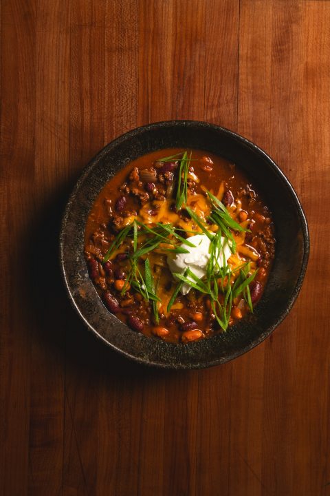 A bowl of chili with kidney beans, melted cheese, sour cream and green onions