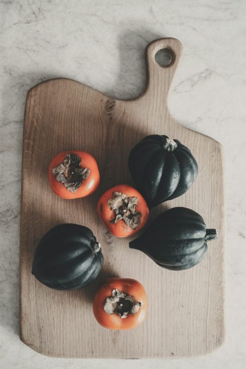 Three dark green acorn squashes and orange persimmons on a wooden cutting board
