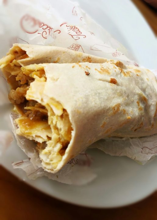 A breakfast burrito wrapped in paper on a plate
