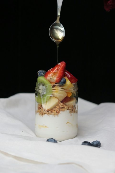 A spoon drizzling fruit into a jar of yogurt